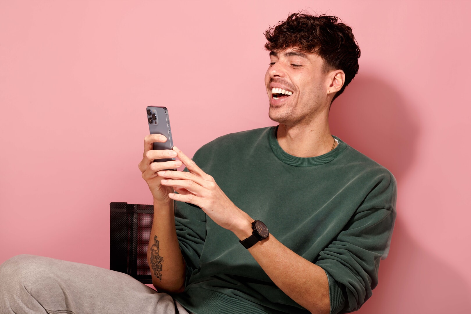 Lachende man met wit gebit tegen roze achtergrond, kijkt op zijn smartphone – voorbeeld van iemand die kiest voor voeding die je tanden niet verkleurt.